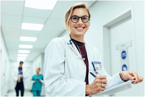Uśmiechnięta lekarka stoi na szpitalnym korytarzu z dokumentami w ręku